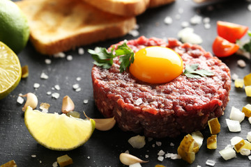 Beef tartare with egg yolk on a black wooden table - obrazy, fototapety, plakaty