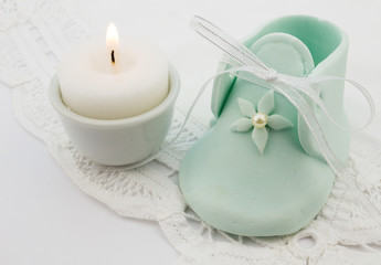 Fototapeta na wymiar Turquoise baby fondant shoe with candle on white lace background