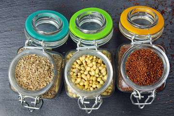 Aromatic spices of coriander seeds, mustard seeds and carom seeds in glass jars on a grey background.
