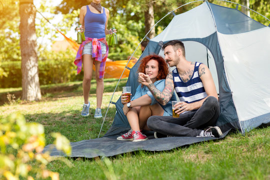 Tattooed guy and lassie sits and drinks beer in front of tent