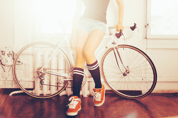 Naklejka premium Young woman on white retro bicycle in studio. The sunlight from the window. Close-up on bike