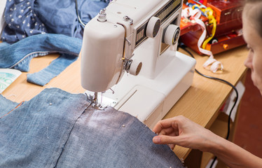 young woman sews on the sewing machine denim