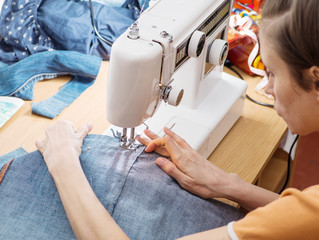 Obraz na płótnie Canvas young woman sews on the sewing machine denim