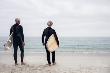 Rear view senior couple in wetsuit holding a surfboard - Powered by Adobe