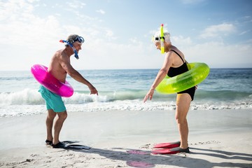 Senior couple with scuba gear and inflatable ring enjoying their holidays on beach - Powered by Adobe