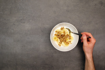 Eating banana dessert with yogurt, walnuts and honey. Top view on healthy breakfast on grey kitchen table. 
