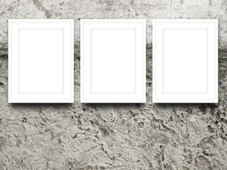 Close-up of three white blank picture frames on rough concrete wall background