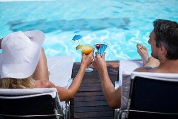 Rear view of couple toasting martini glass while relaxing on sun lounger near pool
