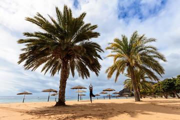 Fototapeta na wymiar Summer yoga session on beautiful de Las Teresitas beach with gold sand brought from Sahara desert - tropical Tenerife island, Canary in Spain. Vriksha-asana, tree pose 