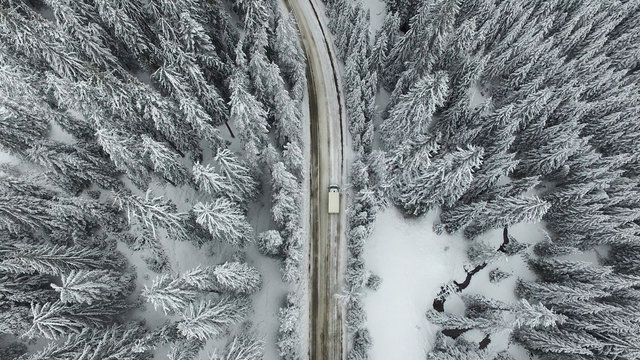 Curving Winding Snowy Road with a Car in the Forest