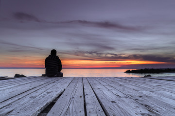 Naklejka na ściany i meble Man sitting on the pier and watching the sunset