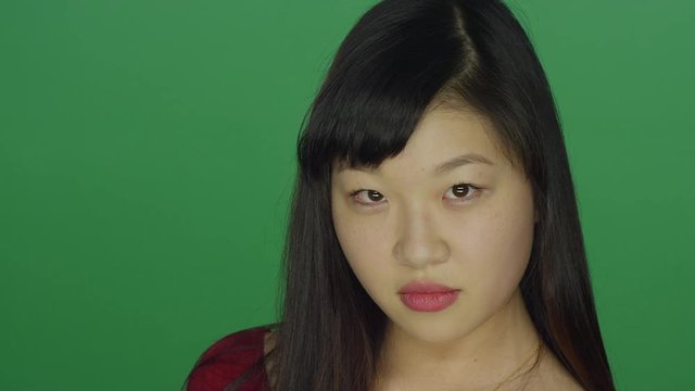 Young Asian woman turns around and stares at the camera, on a green screen studio background