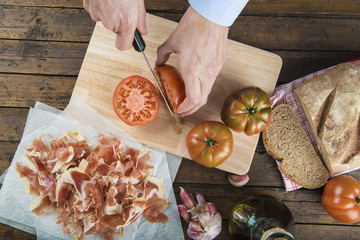 Cocinero cortando el tomate y el pan para preparar tostas tradicionales de jamón con pan tumaca