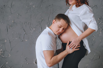 Man is embracing stomach of a pregnant woman. There is a place for Tex. On a gray background.  She...