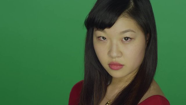 Young Asian woman turns around and stares at the camera, on a green screen studio background