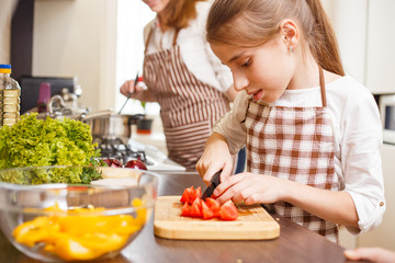 Small teenage girl cutting tomatoes in salad