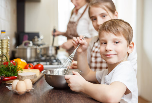 Smiling small boy whisking eggs in bowl on table