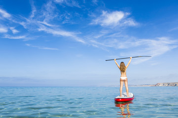 A beautiful and happy woman with arms up and learning paddle-sur