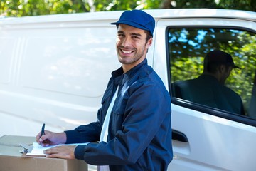 Portrait of happy delivery person writing in clipboard 