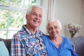 Senior couple sitting with arms around on sofa