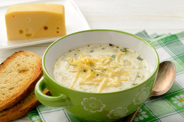 Potato soup with cheese on white wooden table.