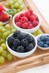 fresh berries and green grapes on a wooden tray, vertical