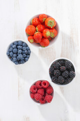 Fresh berries in a  bowl on white wooden background, vertical