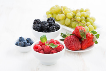 Fresh berries in bowls and green grapes on a white wooden table