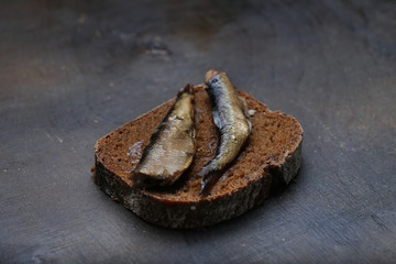 Snacks with sardines on black rye sliced bread. Riga traditional delicious dish. Smoked sprats on dark background.