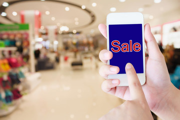 hand hold mobile phone blurred in shopping mall background