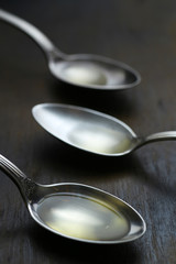 Olive oil in the spoons on wooden background. Close up