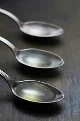 Olive oil in the spoons on wooden background. Close up