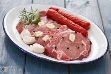 pork with smoked sausages and garlic on dish on blue wooden background