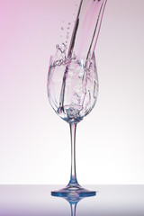 Water with pink tint pouring into a wineglass with splashes.