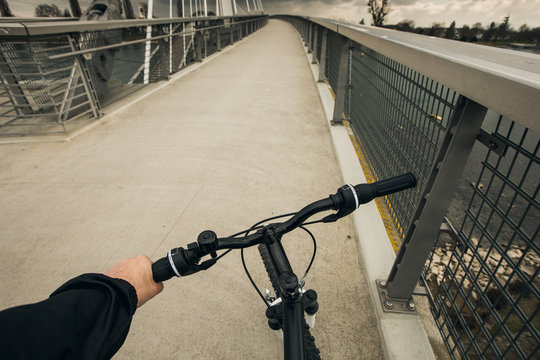 Close-up image of cyclist man hands on handlebar riding bike in park, face is not visible.Young man riding bike in city park over a bridge.View from bikers eyes.