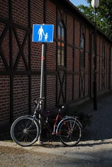 Bicycle standing next to a crosswalk sign with building in the background