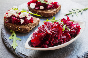 Toasts on the dark slate (stone) background. Cheese, beet and arugula.