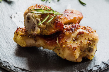 Roasted chicken legs and rosemary on the black background. Cooked with sauce from mustard, orange,...