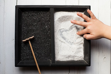 Close up of a boy drawing heart shape in sand 