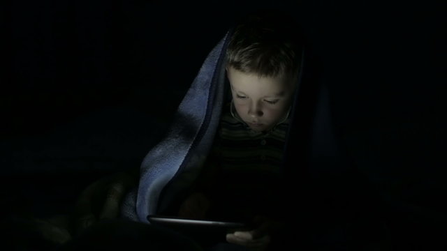 The boy with the tablet under the blanket