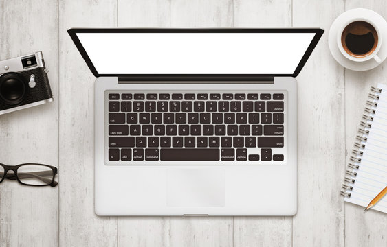 Laptop with isolated white screen for mockup. Work desk with camera, glasses, coffee, notepad and pencil beside on wooden table. Top view.