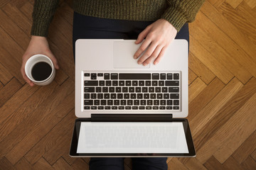 Woman using laptop, drinking coffee and sitting on a wooden flor. Working at home.