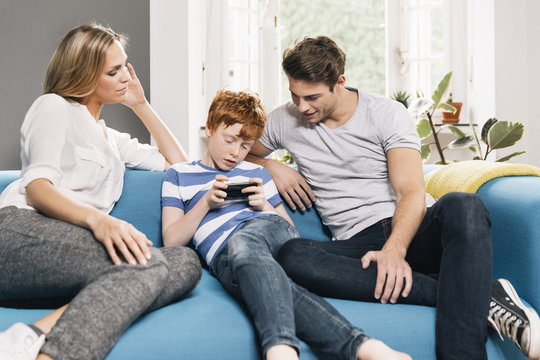 Young family sitting on couch looking at smartphone