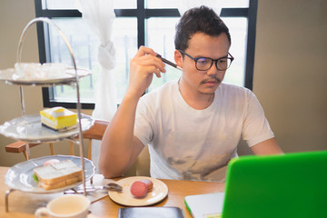 A man and his computer with thinking face at tea time / A man is working with his computer pen and thinking with his work at tea time with tea set and sandwich and snack