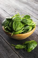 Spinach leaves in bowl on dark wooden background