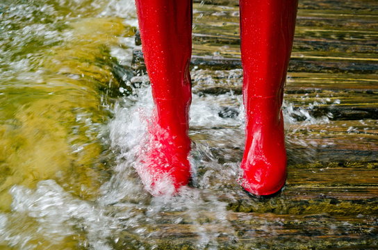 red rubber boots in water on wooden bridge, river overflowed its banks.

