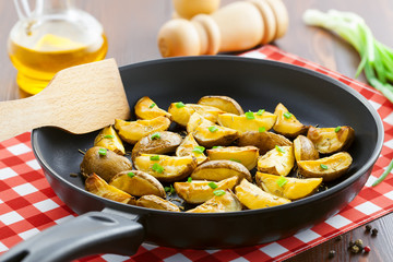 Fresh fried potato wedges with rosemary and spring onion on table