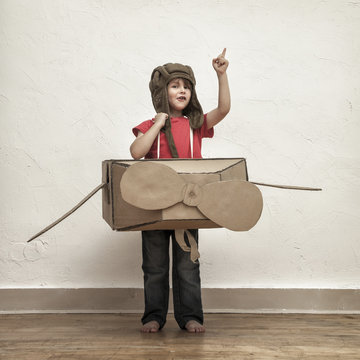Little boy playing with pilot hat and cardboard box airplane
