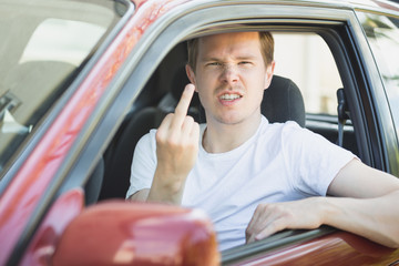 Junger Mann sitzt im Auto und zeigt den Mittelfinger / Vogel