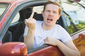 Junger Mann sitzt im Auto und zeigt den Mittelfinger / Vogel